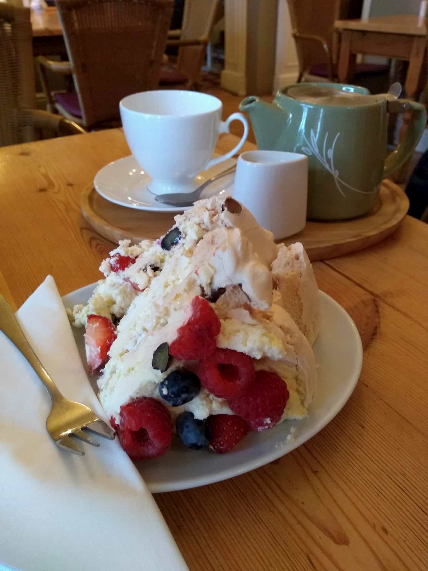 Huge piece of summer fruits meringue and teapot in cafe