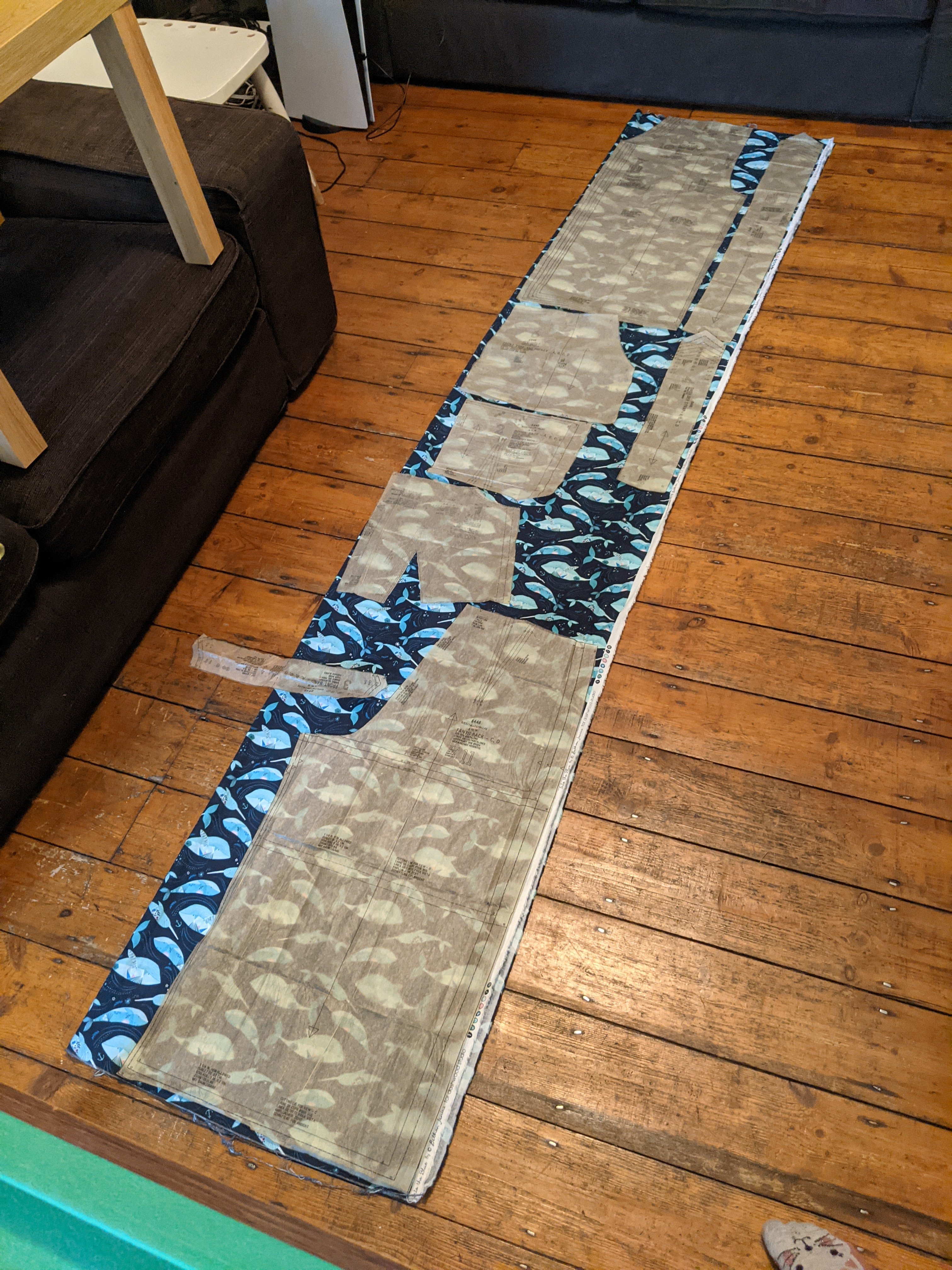Narwhal fabric laid out on the floor, with sewing pattern pieces laid out on top of it, ready for cutting out