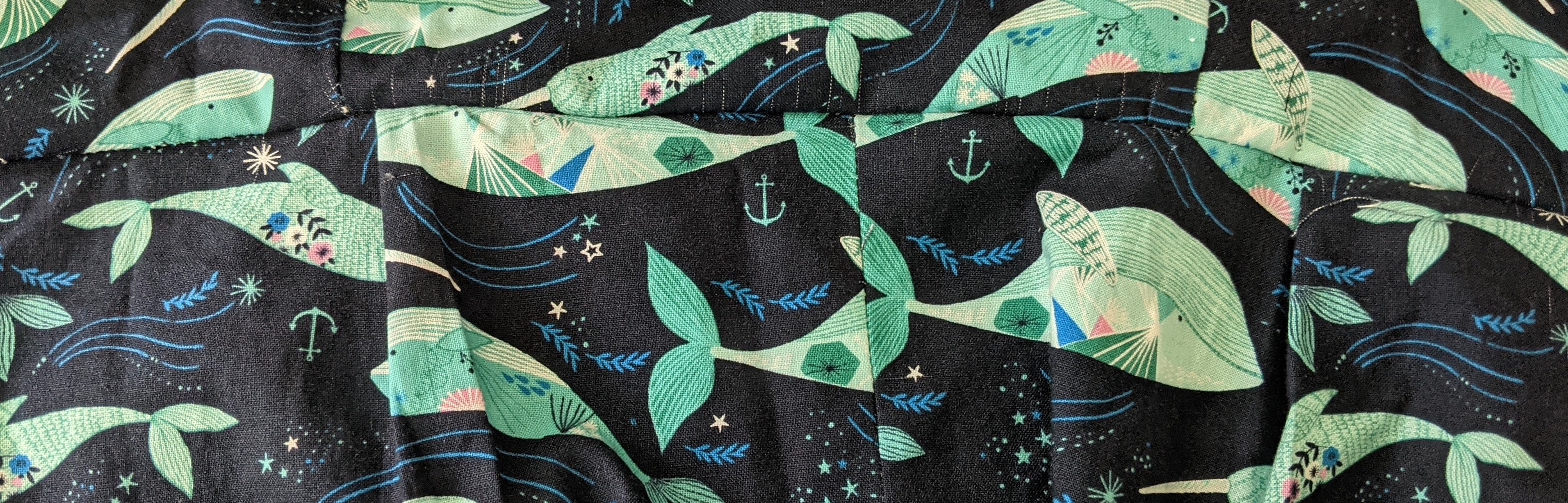 Dark blue fabric with light blue narwhals and whales on it, with little anchors, flowers and stars decorating the space between them