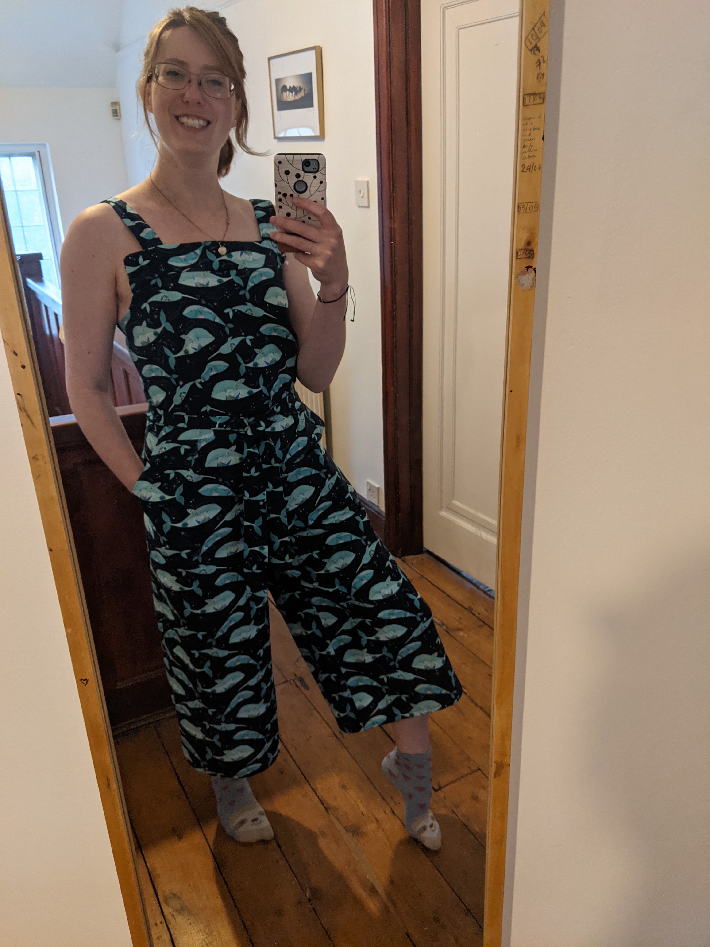 Beverley wearing the jumpsuit made out of the narwhal fabric. Trouser legs are mid-calf length and baggy, and it has a belt around the waist. Photo is a selfie taken in a mirror and Beverley is smiling